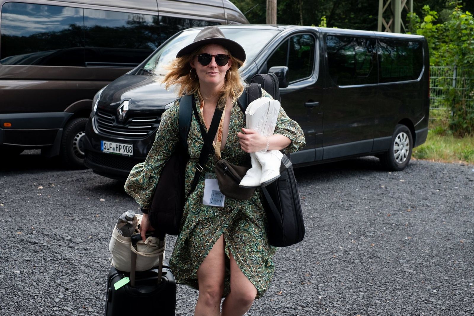 A band member arriving with bags, a ukulele case and a pair of white boots, the tour van behind her
