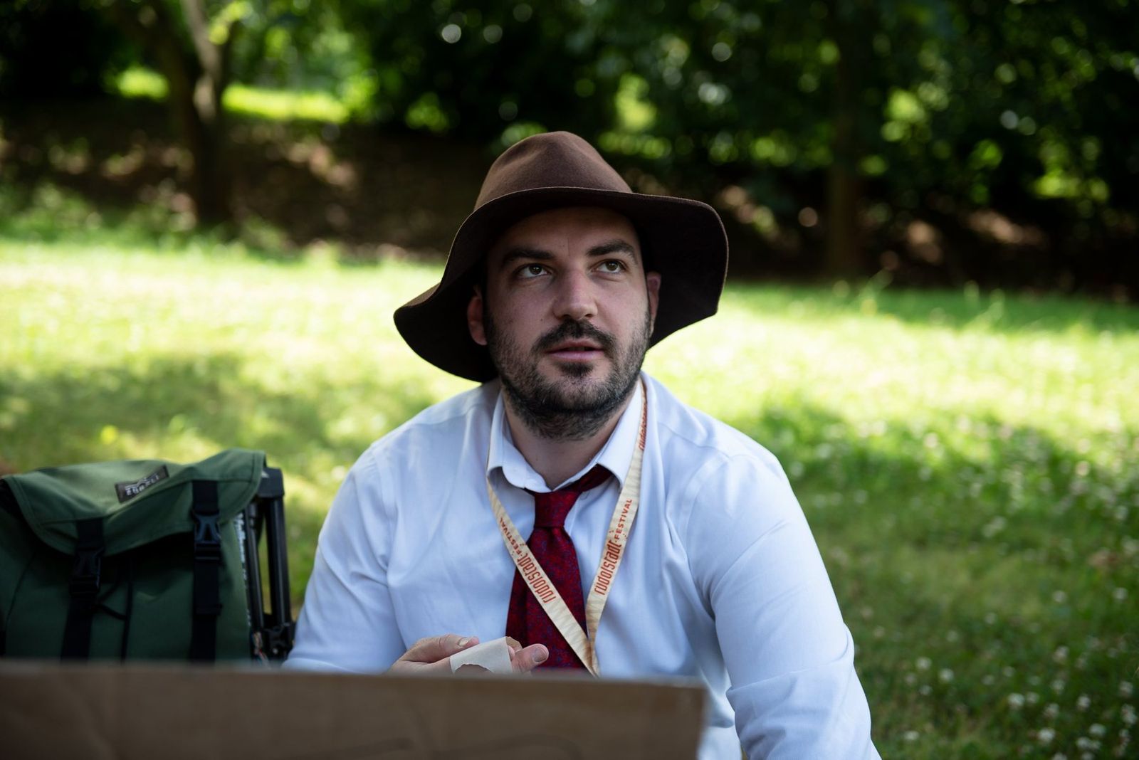 A band member in a hat sitting on the grass beside the costume boxes