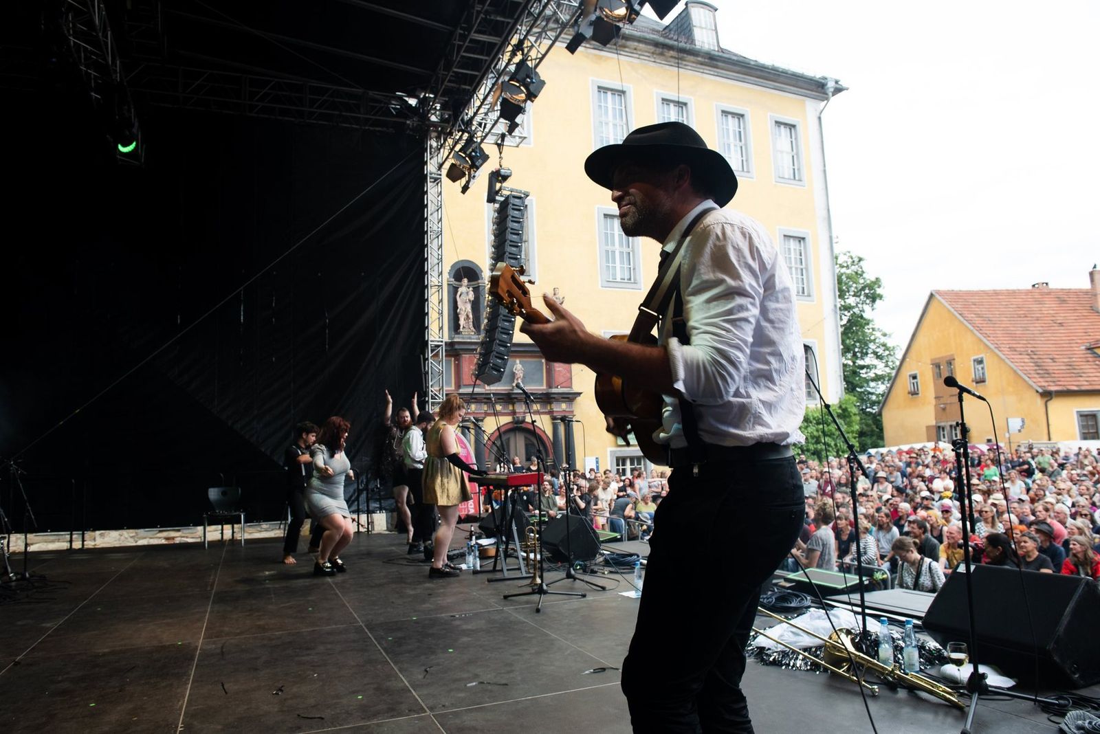 A guitarist in a hat playing towards the crowd at the edge of the stage
