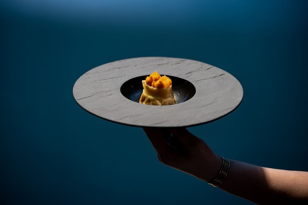 A hand serving a plated dish against a blue wall
