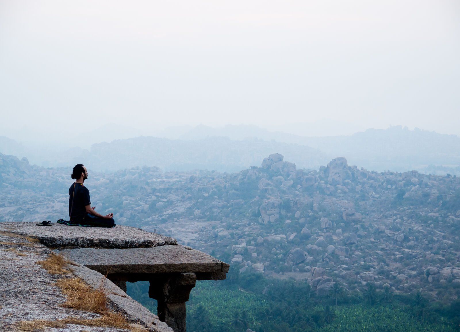 A man meditating on a rock above a misty valley