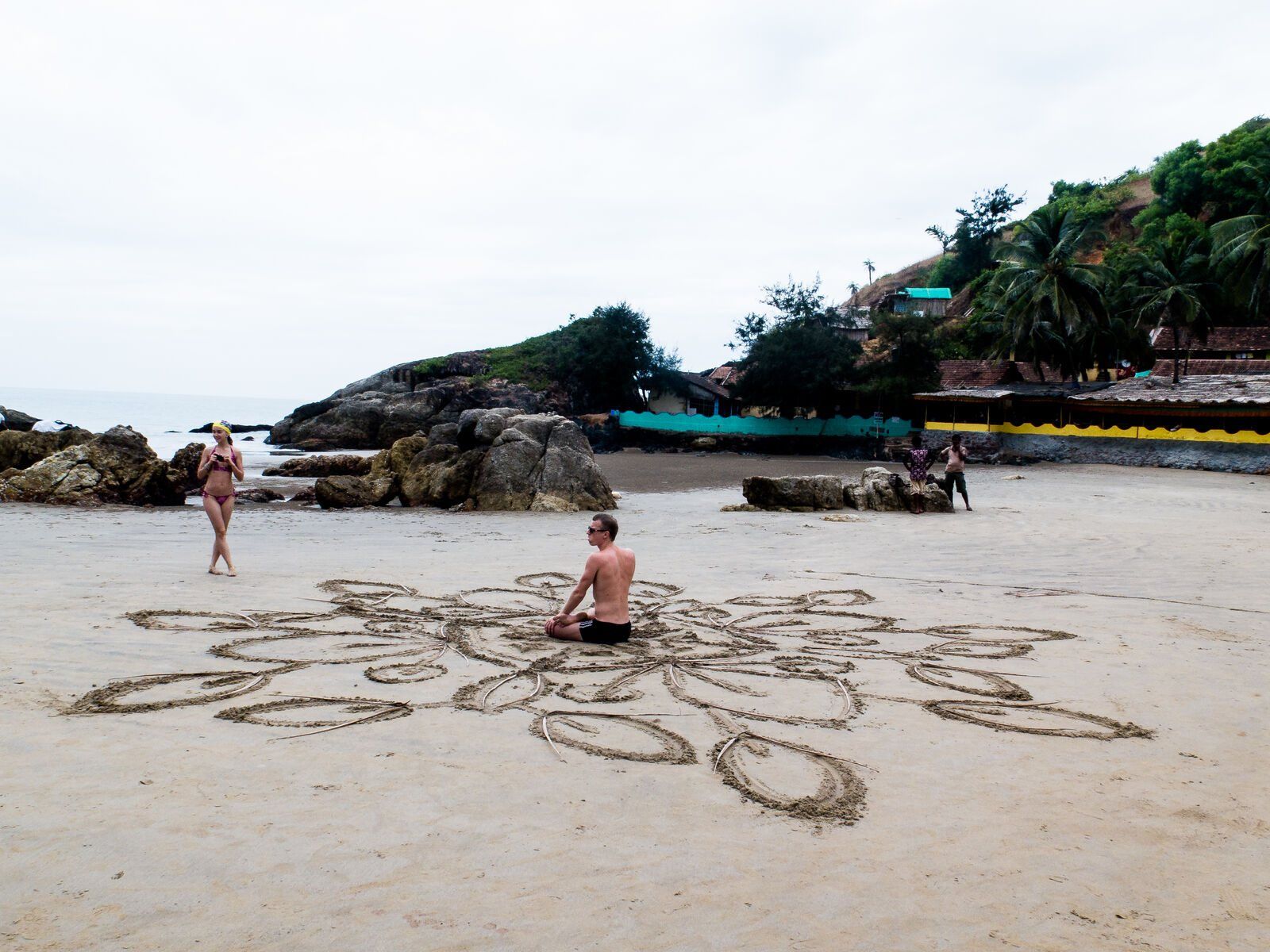 A sand drawing on the beach, a figure sitting in its centre