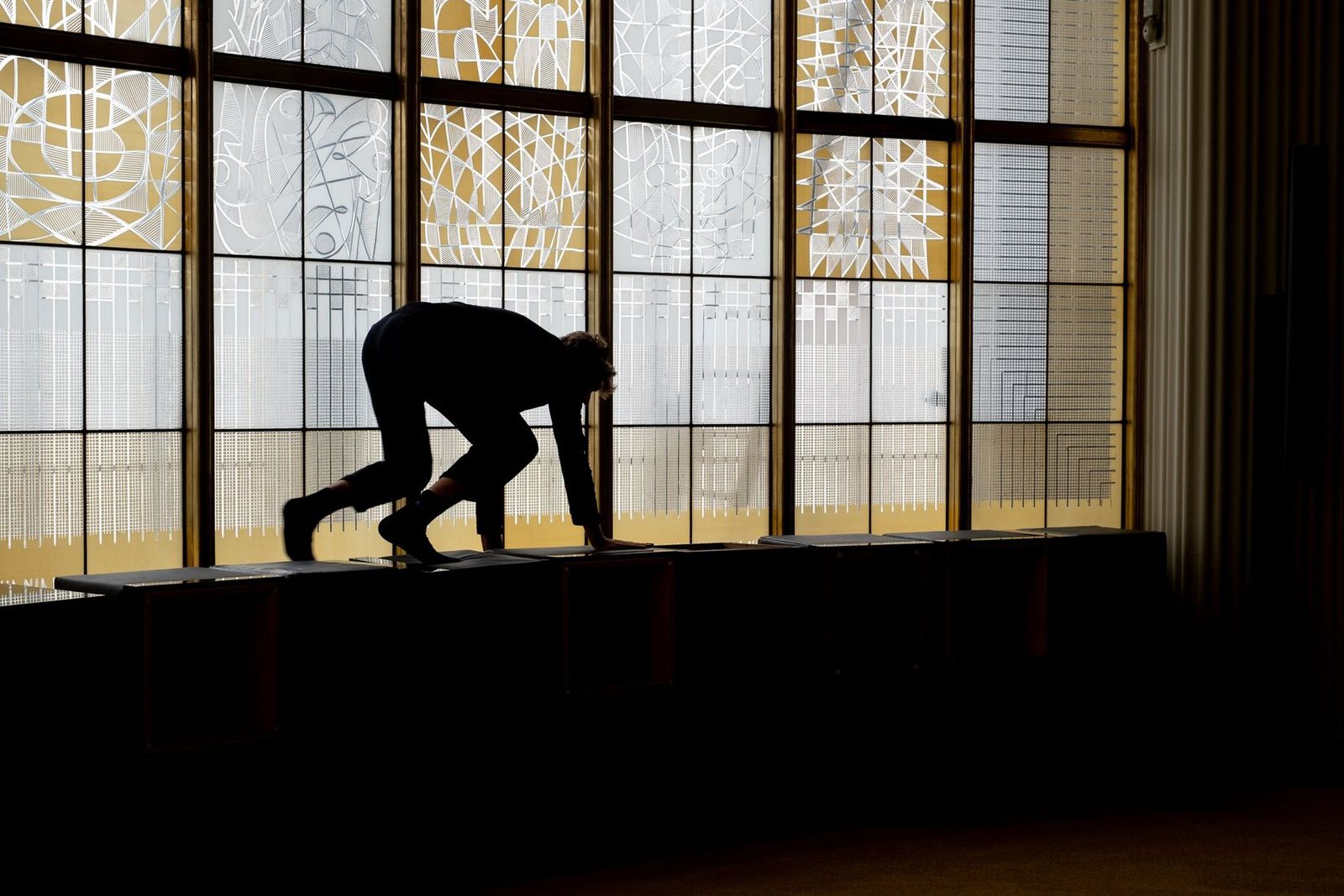 A silhouette climbing along the tall windows of the Schillertheater foyer while the room is set up