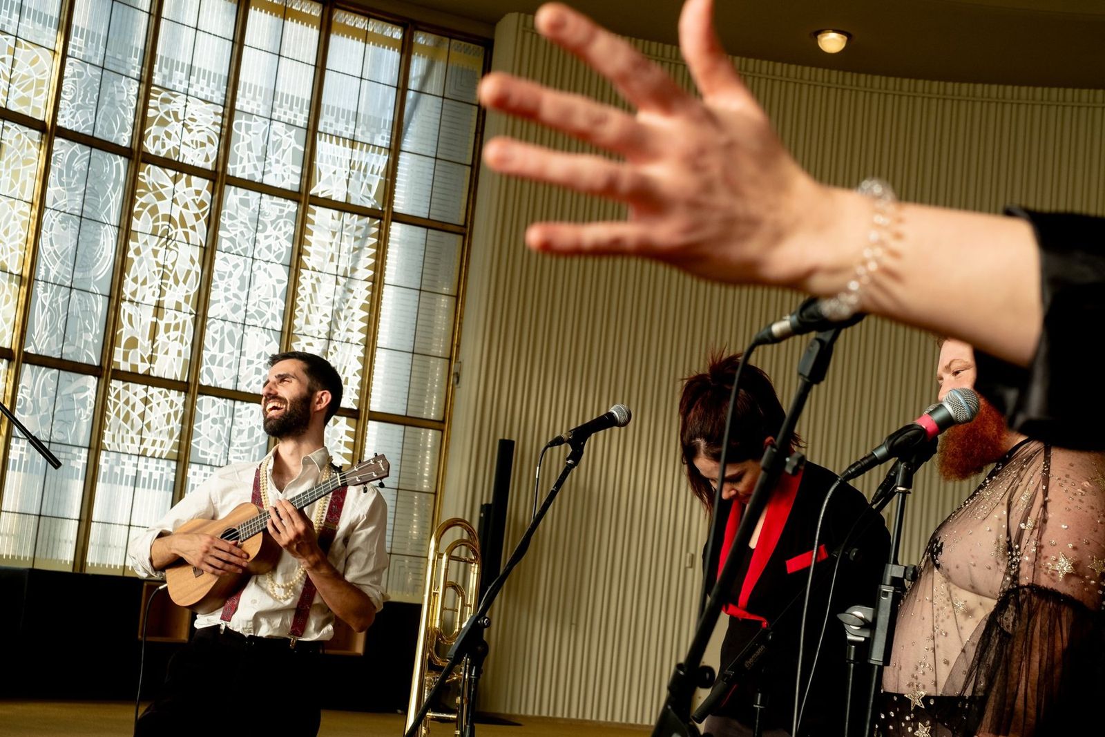 A ukulele player mid-song while a singer reaches across the frame