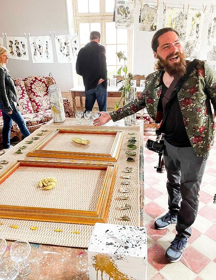 Aaron at the opening of Impressions of Now, gold-leafed objects in frames on a long table