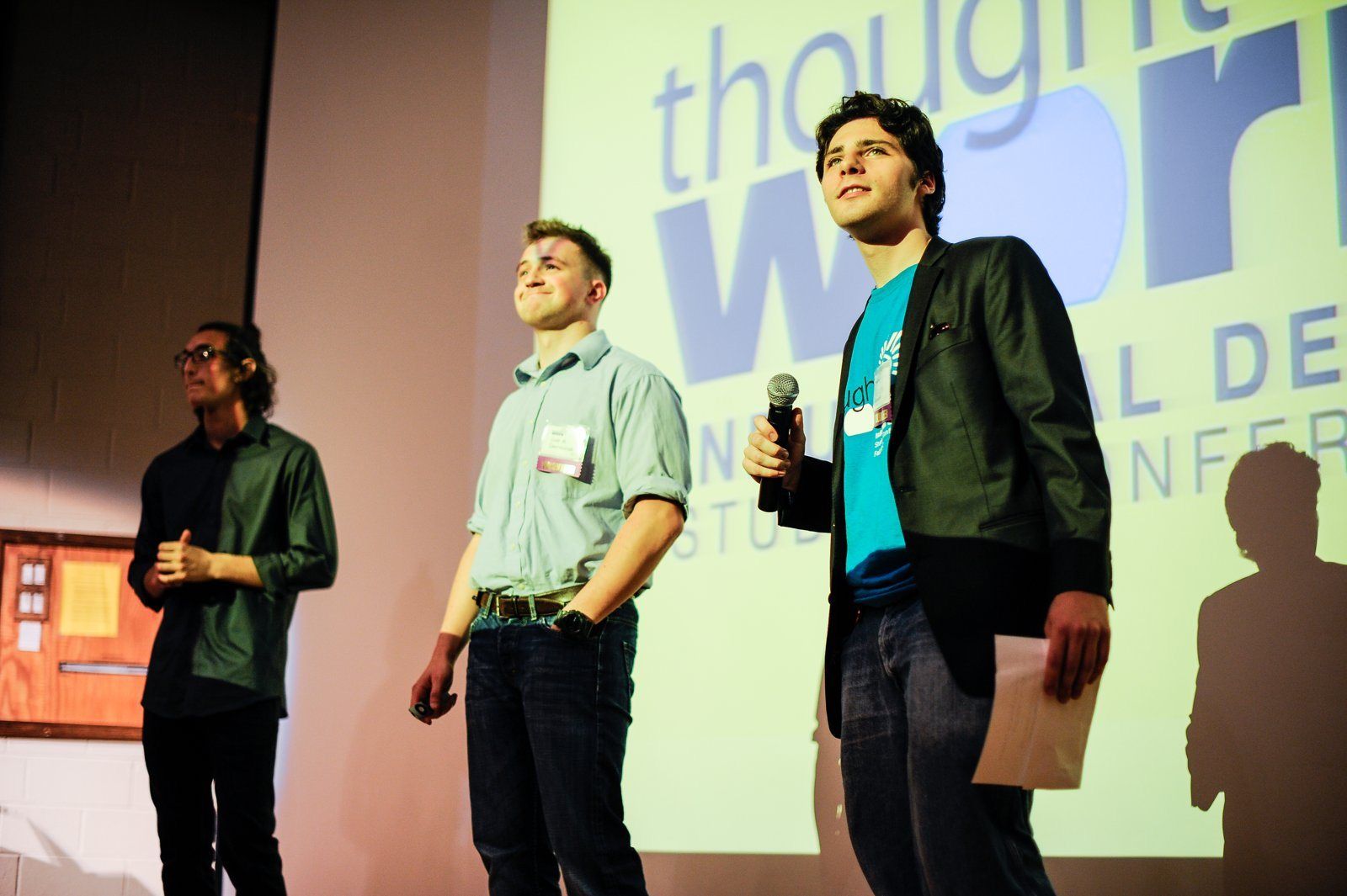 Aaron Jack on stage with a microphone, opening Thought at Work 2012 in front of the conference screen