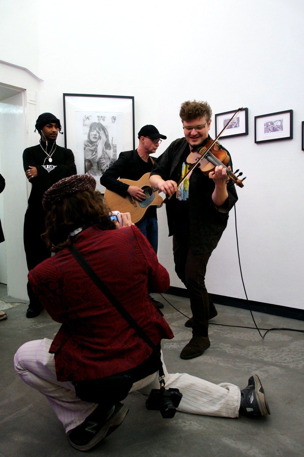 Aaron kneeling to photograph the musicians playing guitar and violin