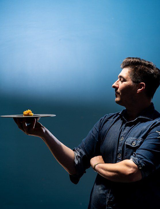 Chef Raul Hennig holding a plate against a blue wall
