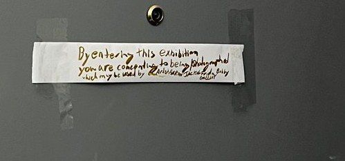 Detail of the handwritten sign: By entering this exhibition you are consenting to being photographed