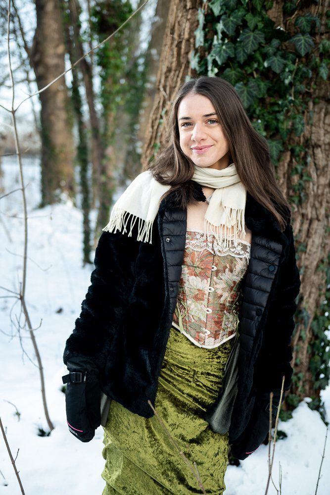 Julia in a fur coat and cream scarf against a tree