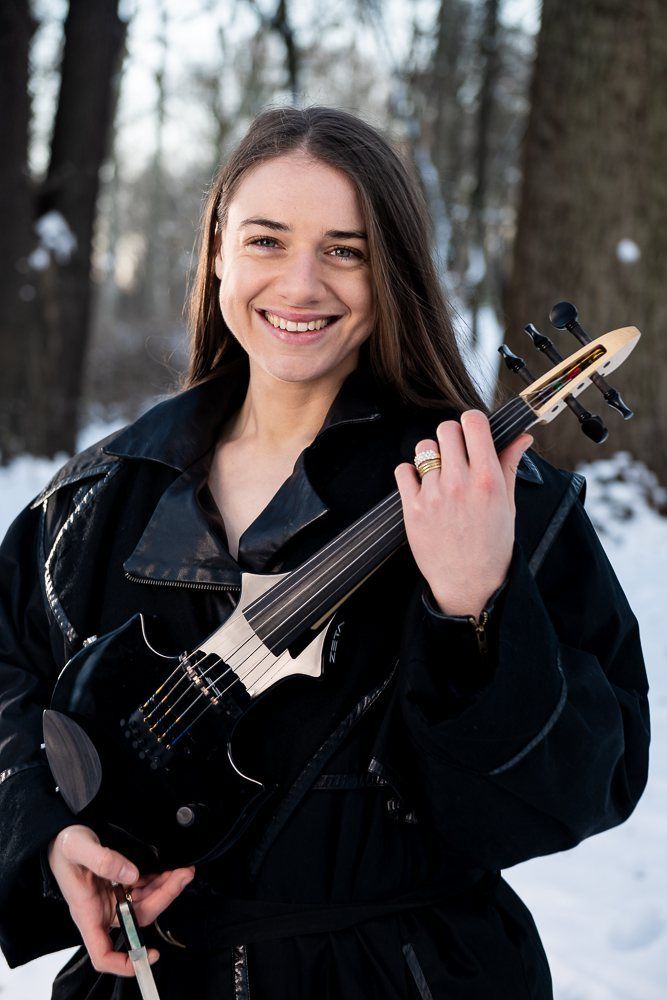 Julia smiling, holding the violin up in a long black coat