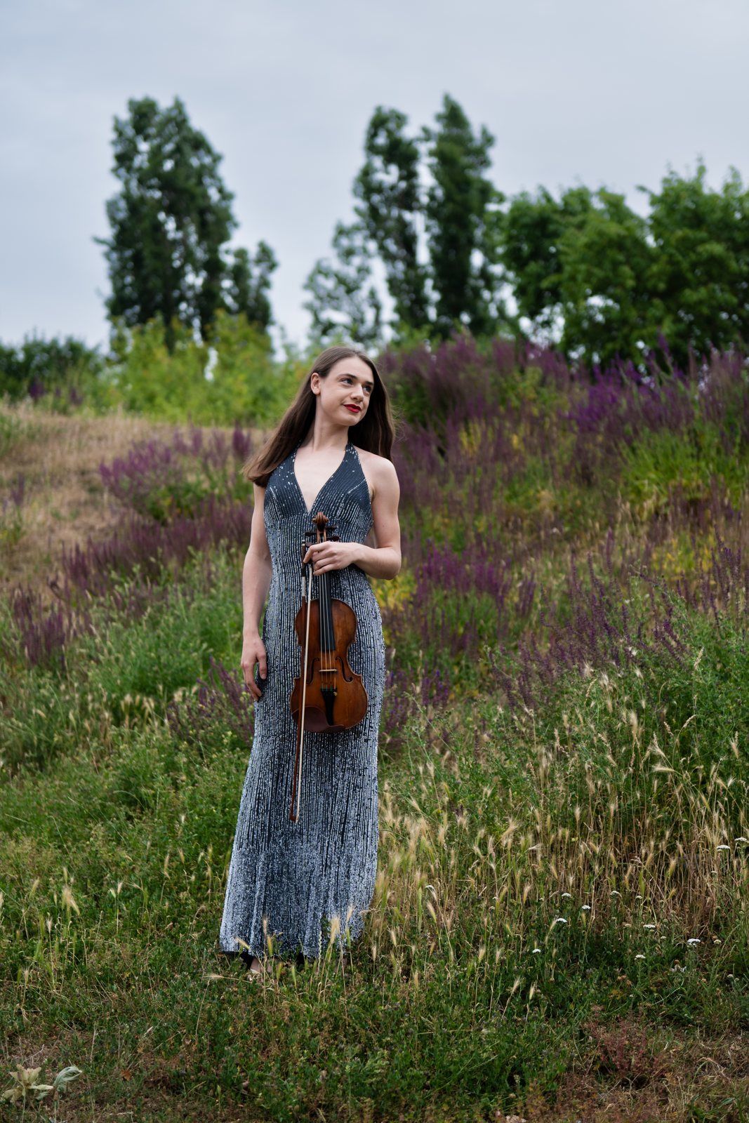 Julia standing in a meadow of purple flowers with her violin