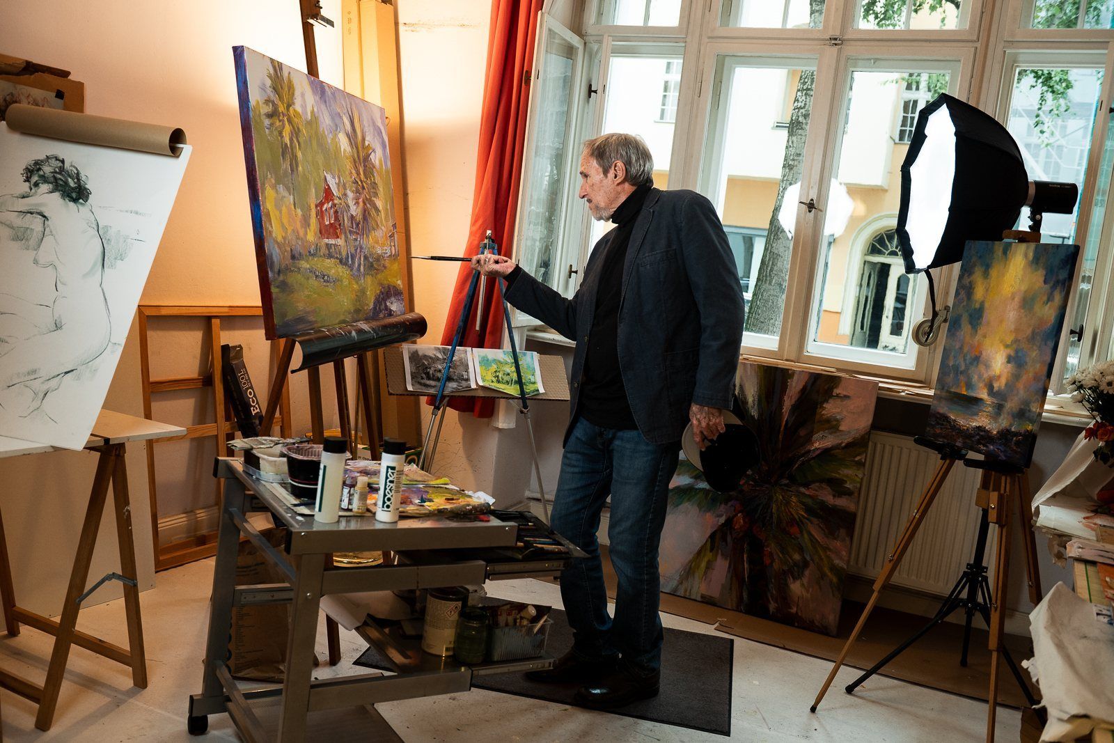 Painting at the easel by the window, studio lights set up