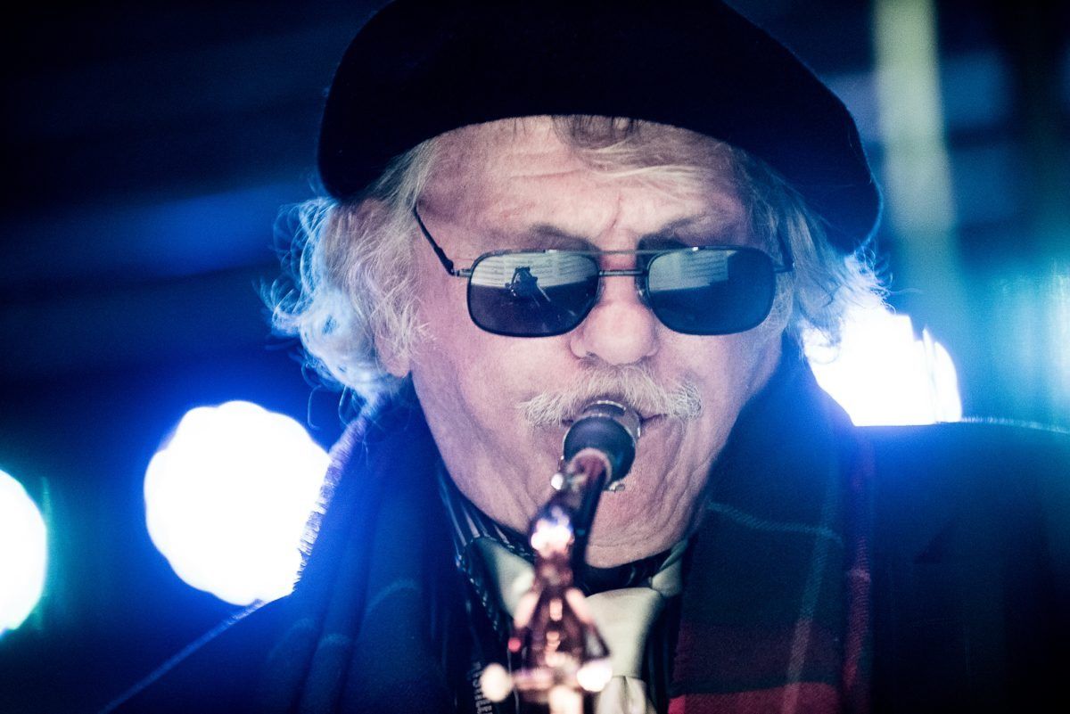 Richie Cole in a beret and sunglasses, singing under blue stage light