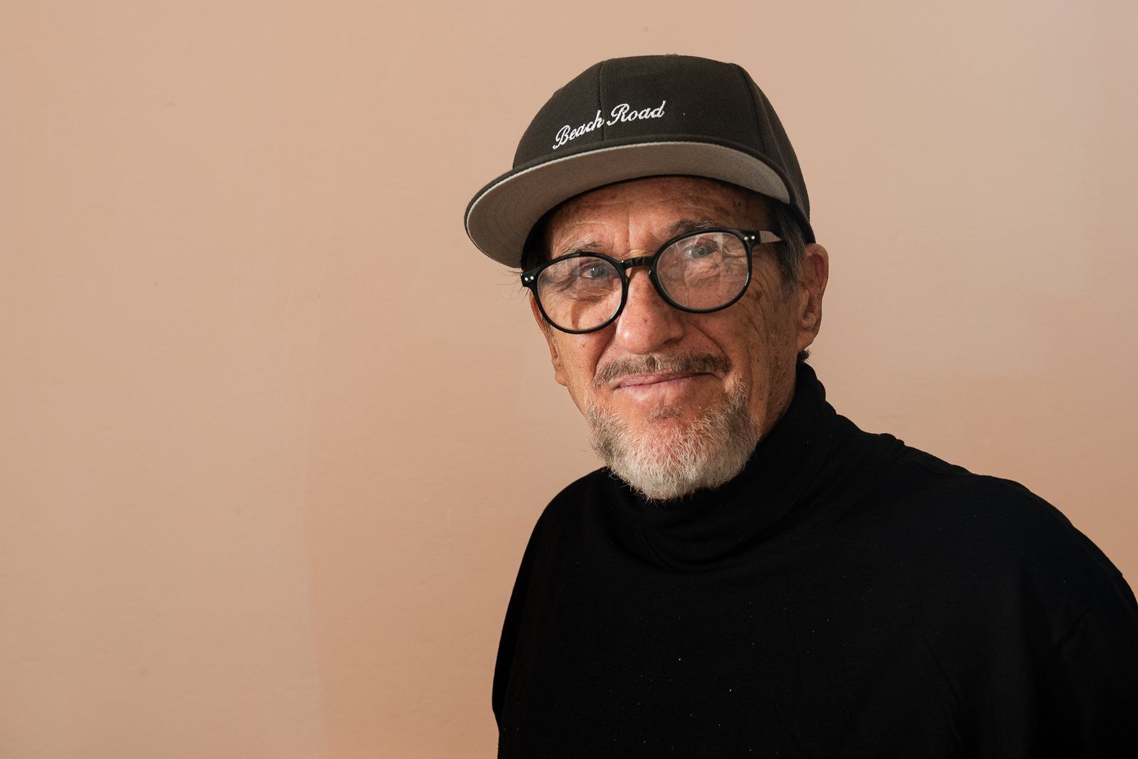 Rod Cameron in a cap and glasses against a warm wall