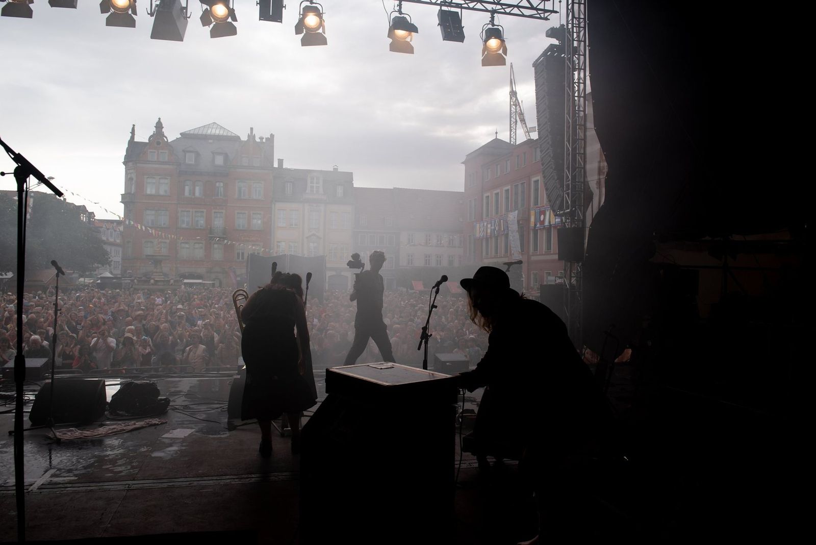 The band in silhouette against the haze, the old town square and the crowd beyond