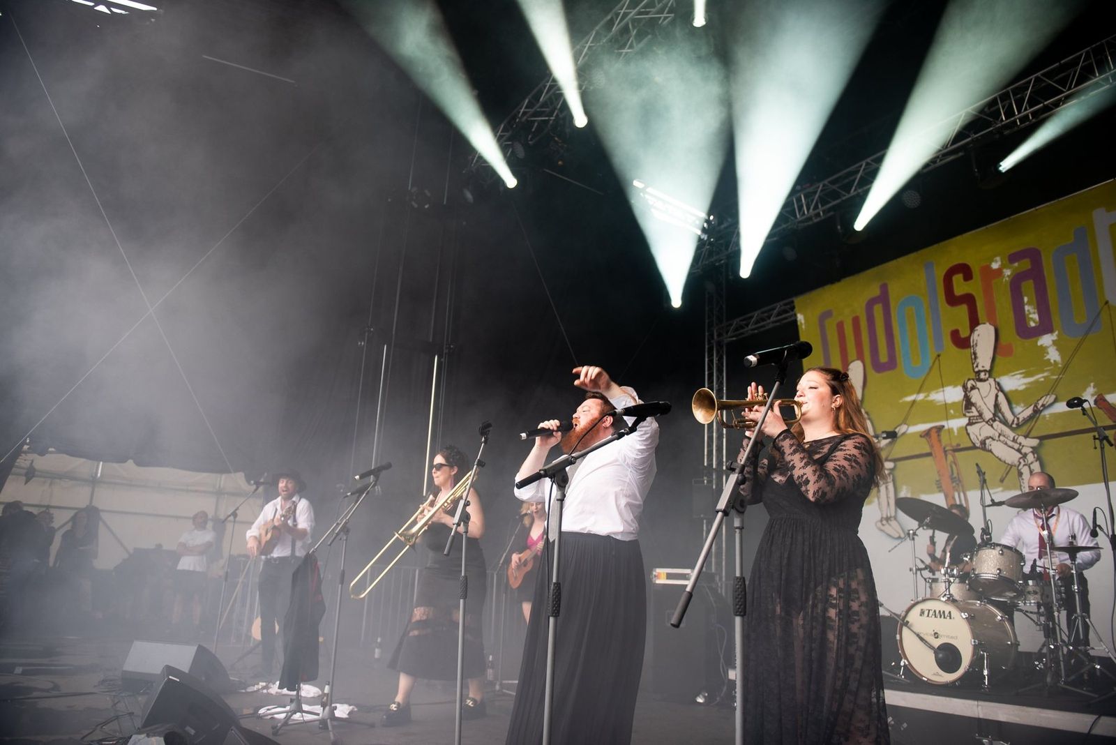 The full band under green stage lights in front of the Rudolstadt Festival banner