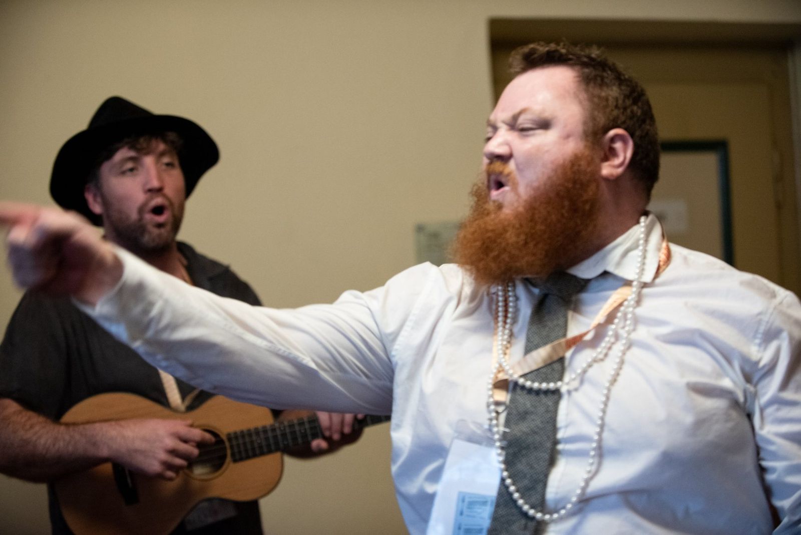 The singer in pearls and a tie belting a line to the room while a ukulele player sings along