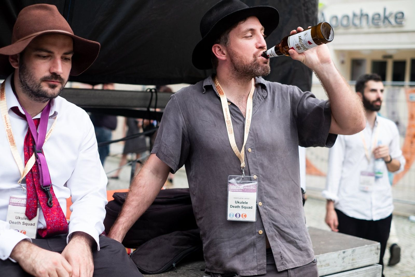 Two band members sitting backstage, one drinking from a bottle
