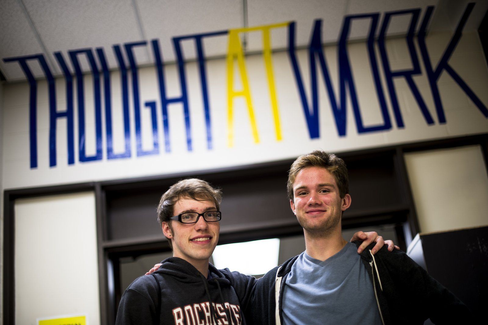 Two students under the Thought at Work wall graphic in the design studio